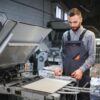 Printing house interior with modern offset print machine and operator in working uniform