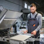 Printing house interior with modern offset print machine and operator in working uniform